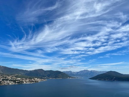 White cirrus clouds in the blue sky over a mountain range near the sea.