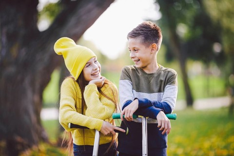 Two children caucasian boy and girl twins posing with scooters in autumn park. Happy kids riding