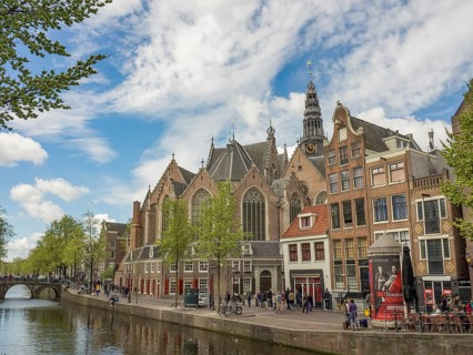 View of a canal with historic buildings and a church under a partly cloudy sky, Amsterdam,