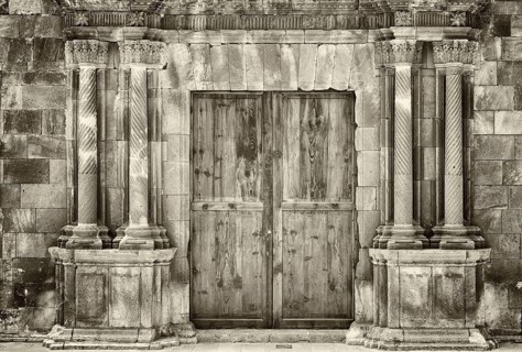 Monochrome sepia ancient wooden double doors in an old stone building with crumbling ornate columns