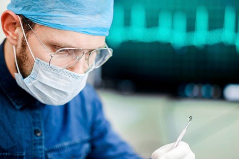 A surgeon in protective gear handling a medical instrument with an ECG in the background