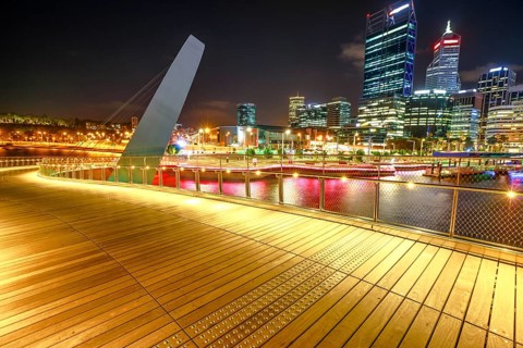 Wooden walkway of Elizabeth Quay pedestrian bridge illuminated by night at Elizabeth Quay marina, a