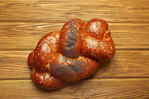 Freshly baked Challah bread covered with poppy and sesame seeds, top view on rustic wooden