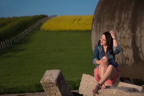 Attractive girl, casual dressed, with bare feet, eyes closed and smiling, sitting on a rock, in