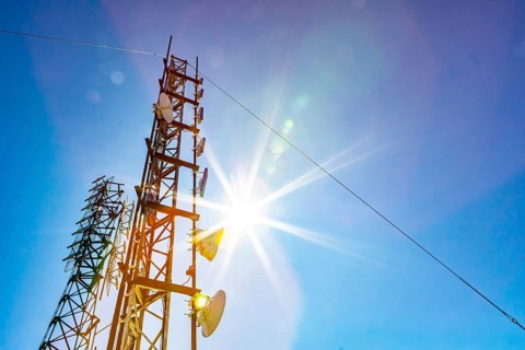 A low angle view of two mobile communication data transmitter and GPS signal towers, against a blue
