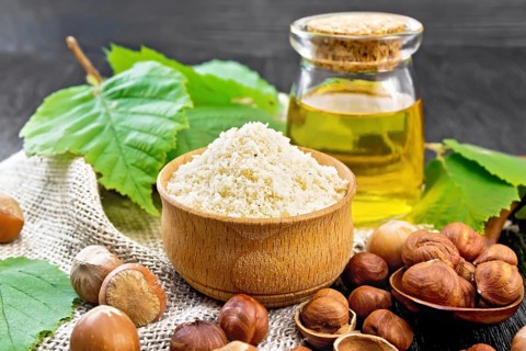 Hazelnut flour in a bowl, nuts in a spoon, oil in glass jar and filbert branch with green leaves on