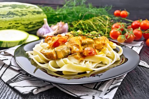 Tagliatelle pasta with meat goulash, tomato, zucchini and thyme in a plate on napkin, garlic, spicy