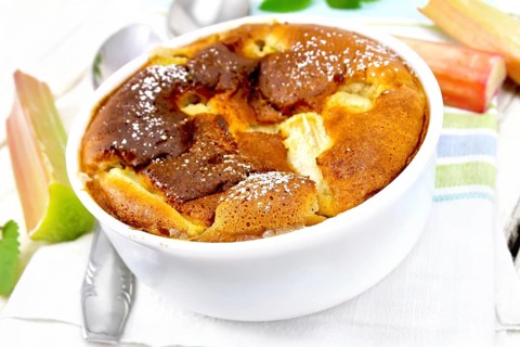 Pie klafouti with rhubarb in the bowl, mint and rhubarb stalks on a napkin against light wooden