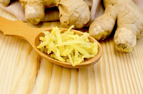 Wooden spoon with grated ginger, ginger root on a napkin on the background of wooden board