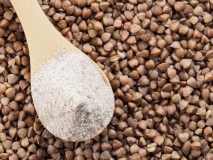 Buckwheat flour in wooden spoon and buckwheat grains. Whole-grain buckwheat flour on buckwheat