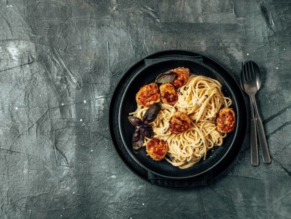 Zucchini Parmesan Meatballs with Pasta Carbonara in black craft plate over gray background. Close