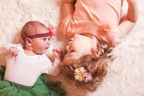 Little girl with her newborn sister on a fur carpet