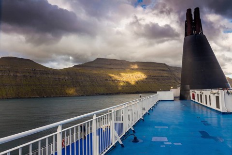 Blue sun deck of a ferry with the coast of the Faroe Islands in the background