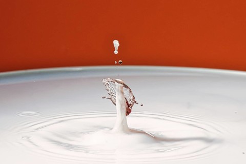 A drop hits a white liquid and creates a splashing movement, water droplets, collision, high-speed