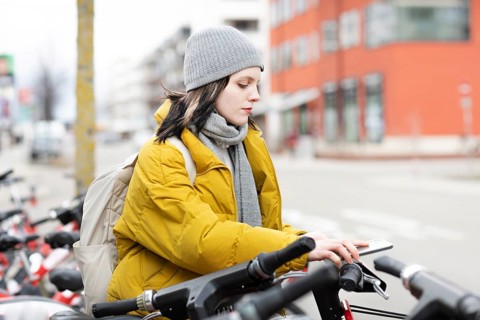 Woman in yellow jacket and cap on rental bikes in city street, cold winter day, environmentally