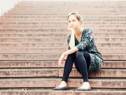 Sad lonely young woman sitting on steps. Portrait of serious girl with facial expression outdoors