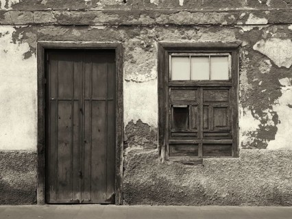 Monochrome image of the front of an old abandoned house with shuttered windows and locked wooden