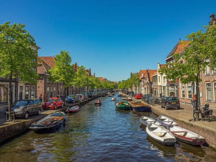 A long canal lined with boats, cars and historic buildings on a sunny day, alkmaar, the netherlands