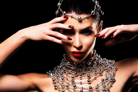 Beautiful woman with dark makeup wearing blue and silver mask surrounded by party accessories on