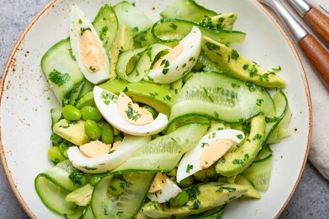 Healthy green avocado salad bowl with boiled eggs, sliced cucumbers, edamame beans, olive oil and