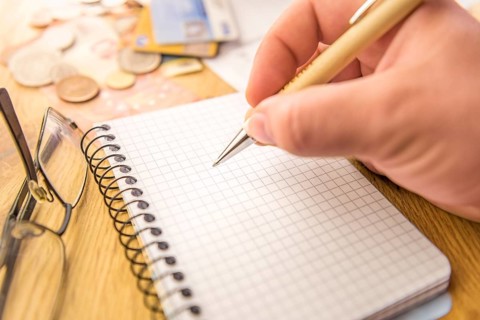Close-up image with a blank math notebook and a man's hand holding a pen. In the background there