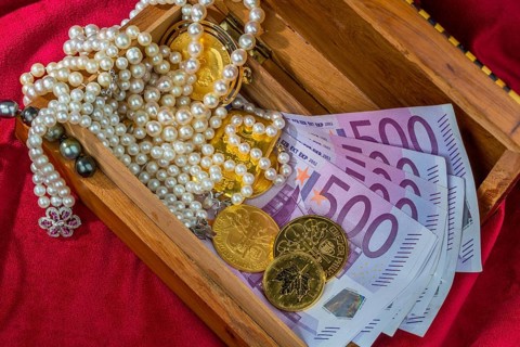 Gold in coins and bars with jewellery on red velvet. Symbolic photo for wealth, luxury, wealth tax.