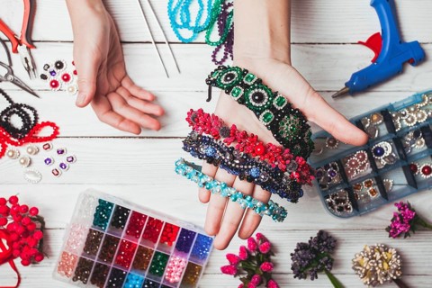 Plastic berries, flowers, beads and instruments for doing handmade headbands. Top view with hands