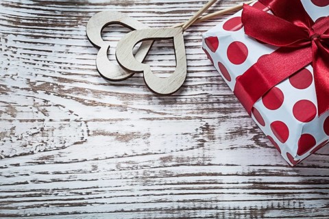 Present box with tied red bow wood hearts on vintage wooden board holidays concept