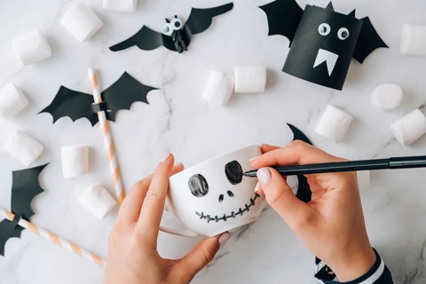 Female hands paint on white cup scary jacks face DIY for kids Halloween home activities Holiday art
