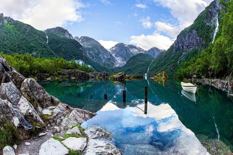 The boat is reflected in the clear water of the lake. Gorgeous Norway. Emerald green of summer