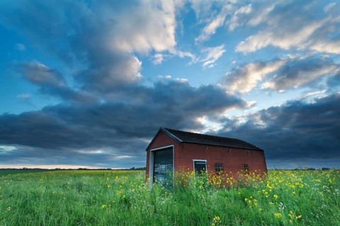Sunset sky over farmhouse on rapeseed field in spring
