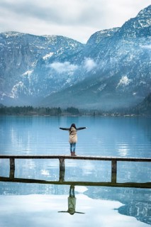 Girl with her arms open, standing on a narrow wooden deck, enjoying the view of the Austrian Alps