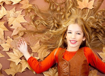 Autumn fall little blond girl on dried tree leaves background and long spread hair