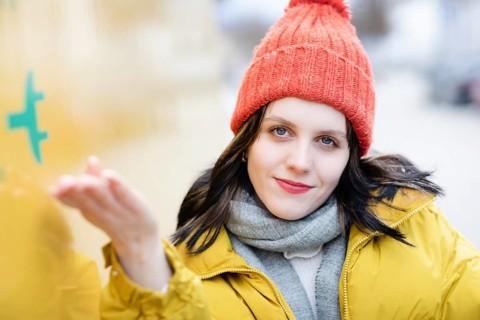 Woman with red hat and yellow jacket points with hand to large electric car for transport, electric