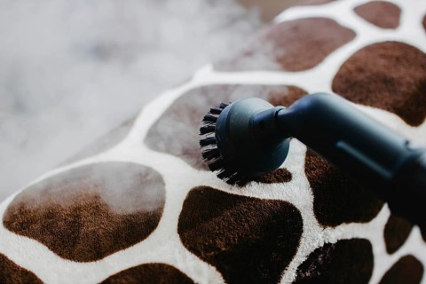 A steam cleaner with a brush head cleaning a giraffe-patterned surface