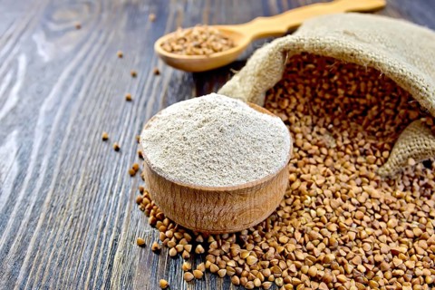 Buckwheat flour in a wooden bowl, buckwheat in a bag on a wooden boards background