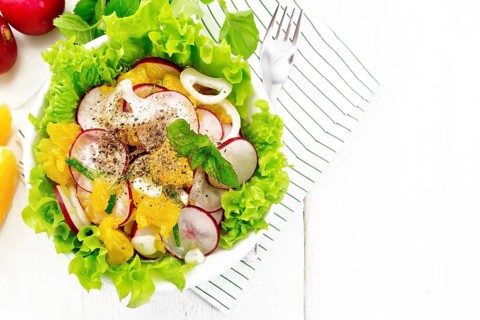 Radish, onion and orange salad with mint, vegetable oil and spices on lettuce in a plate on a towel