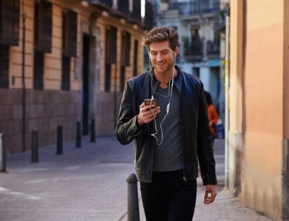 Young man listening music with smartphone earphones walking in the street