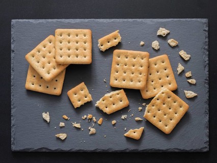 Square crackers with pieces and crumbs on slate gray background. Dry salt cracker cookies with