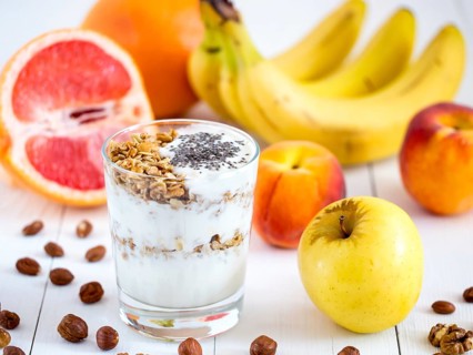 Healthy breakfast: yogurt with muesli and chia seeds, fruits and nuts on white wooden background.