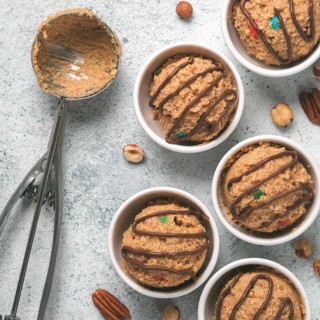 Safe-to-eat raw monster cookie dough in small portion bowl, ice cream scoop and nuts on gray cement
