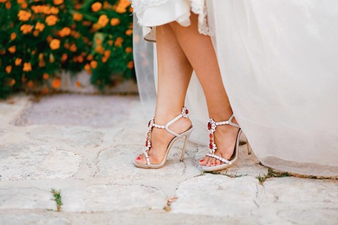 Bride's legs in stylish sandals with crystals with high heels peek out from under the wedding