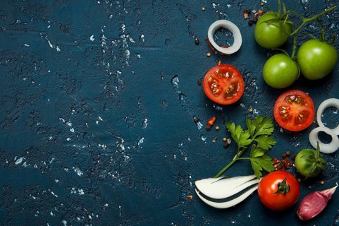 Vegetables background. Fresh vegetables (garlic, tomatoes, onions) on a dark embossed surface. View