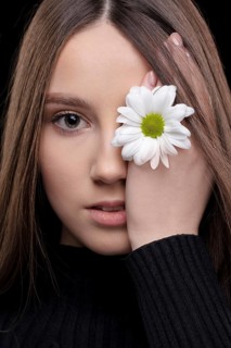 A beautiful girl with natural beauty holds a white flower near her eye. Young girl with a white