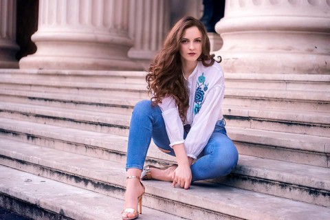 Young girl with brown hair and blue eyes, sits on old marble steps, dressed modern and looking at