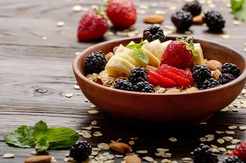 Fruit healthy muesli with banana strawberry almonds and blackberry in clay dish on wooden kitchen
