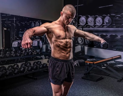 Young handsome sportsman lifting dumbbells in a gym