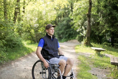 Happy and young disabled or handicapped man sitting on a wheelchair in nature turning wheels on a