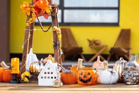 Autumn decor on porch of yellow house outside of pumpkin, lantern, garlands and figure of home and