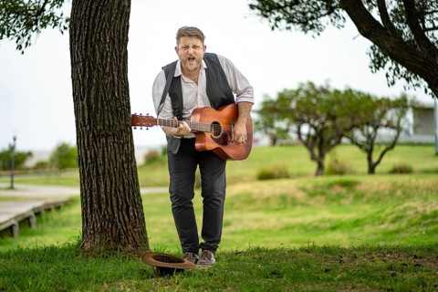 Musician looking at camera while playing guitar and singing in a park